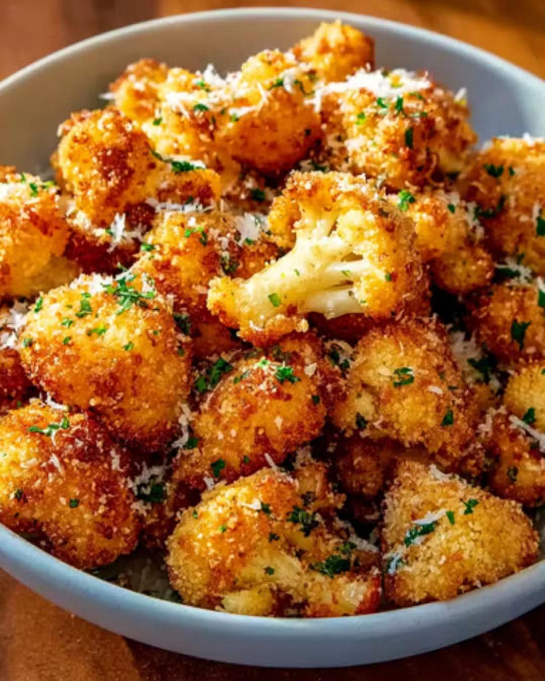Fleurettes de chou-fleur frites et croustillantes, parsemées de parmesan et de persil dans un bol bleu.