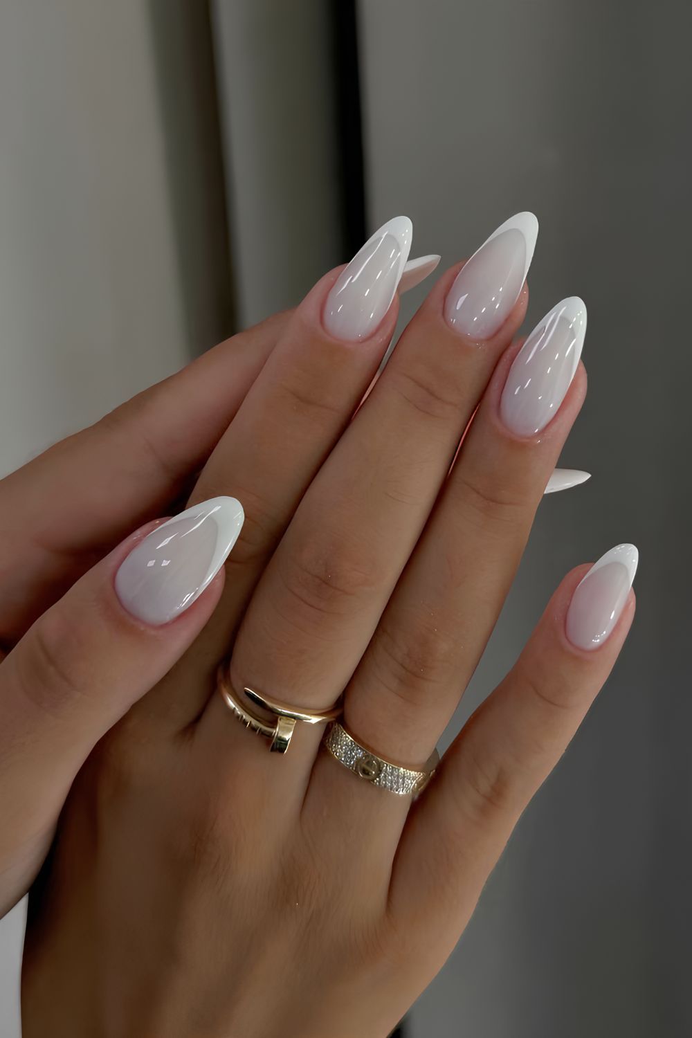 Mains avec ongles longs en dégradé blanc brillant, bagues dorées